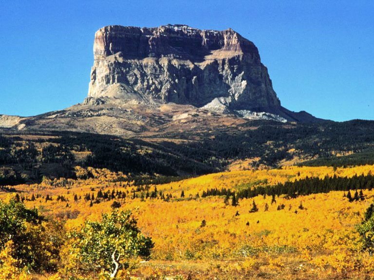 Chief Mountain - A massive stone mountain standing alone and bare surrounded by low scrub and prairieland.