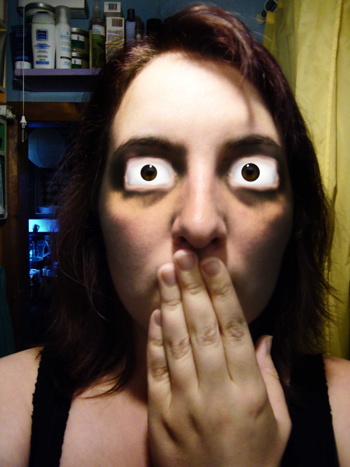 Close up photograph of a woman with her hand over her mouth and bulging square eyes