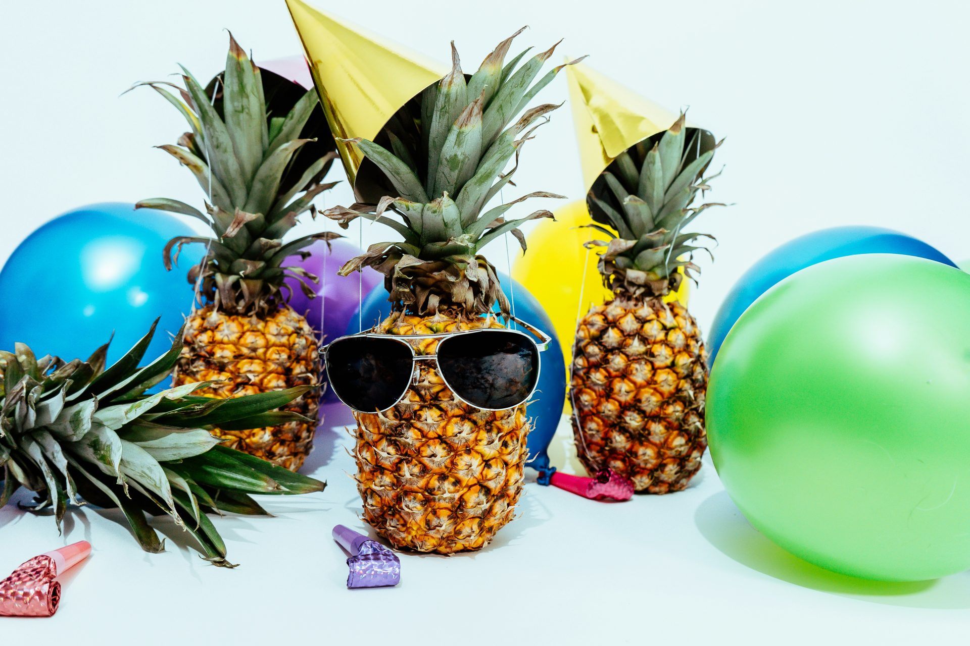 3 pineapples at a party. The center one with sunglasses and all of them wearing party hats