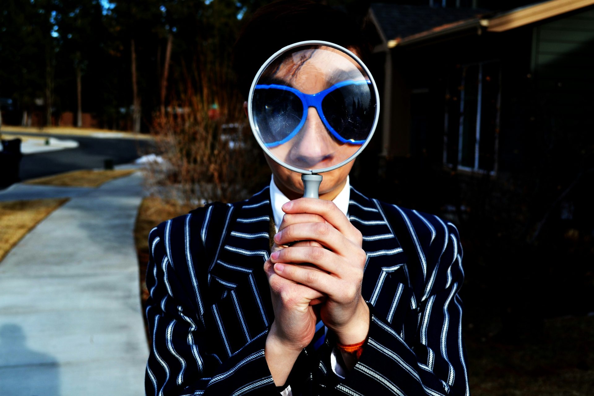 Woman wearing a pinstripe suit with her sunglass protected eyes magnified by a magnifying glass