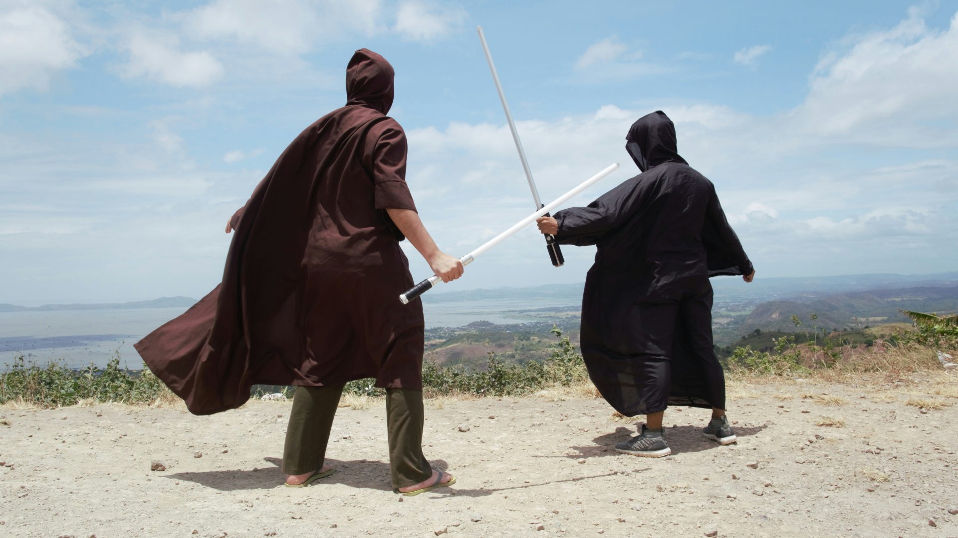 Two teenage guys wearing hoods and capes (one wearing sandals, the other in tennis shoes... no socks for either one) "wielding" plastic light sabers like they are getting ready to duel. On a hill overlooking the ocean. Awesomely pretentious or silly.