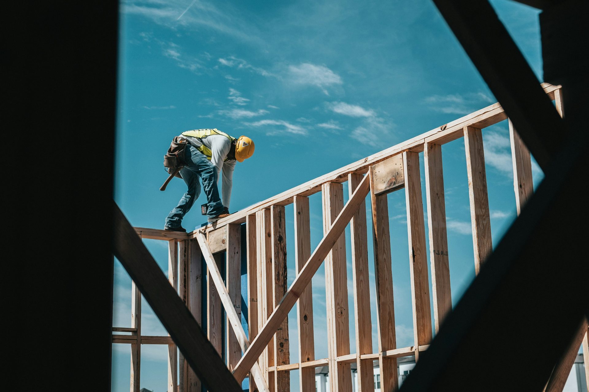 Carpenter balanced on the top of a raw wood wall frame of a house.