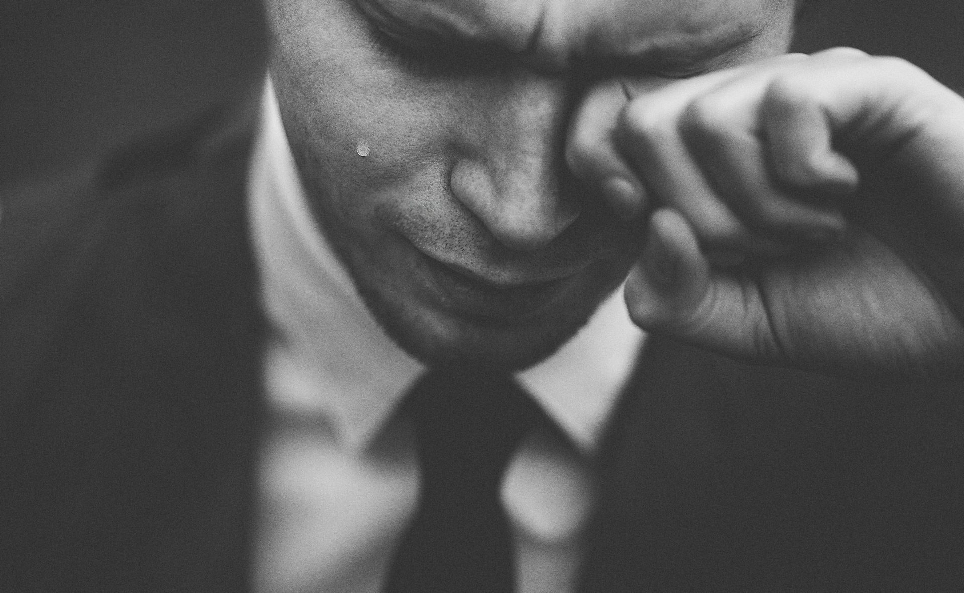 Black and white closeup of man in suit appearing to wipe away tears
