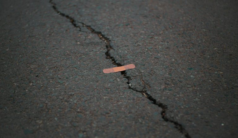 A big crack in an asphalt road with a tiny band-aid across a small part of the gap.
