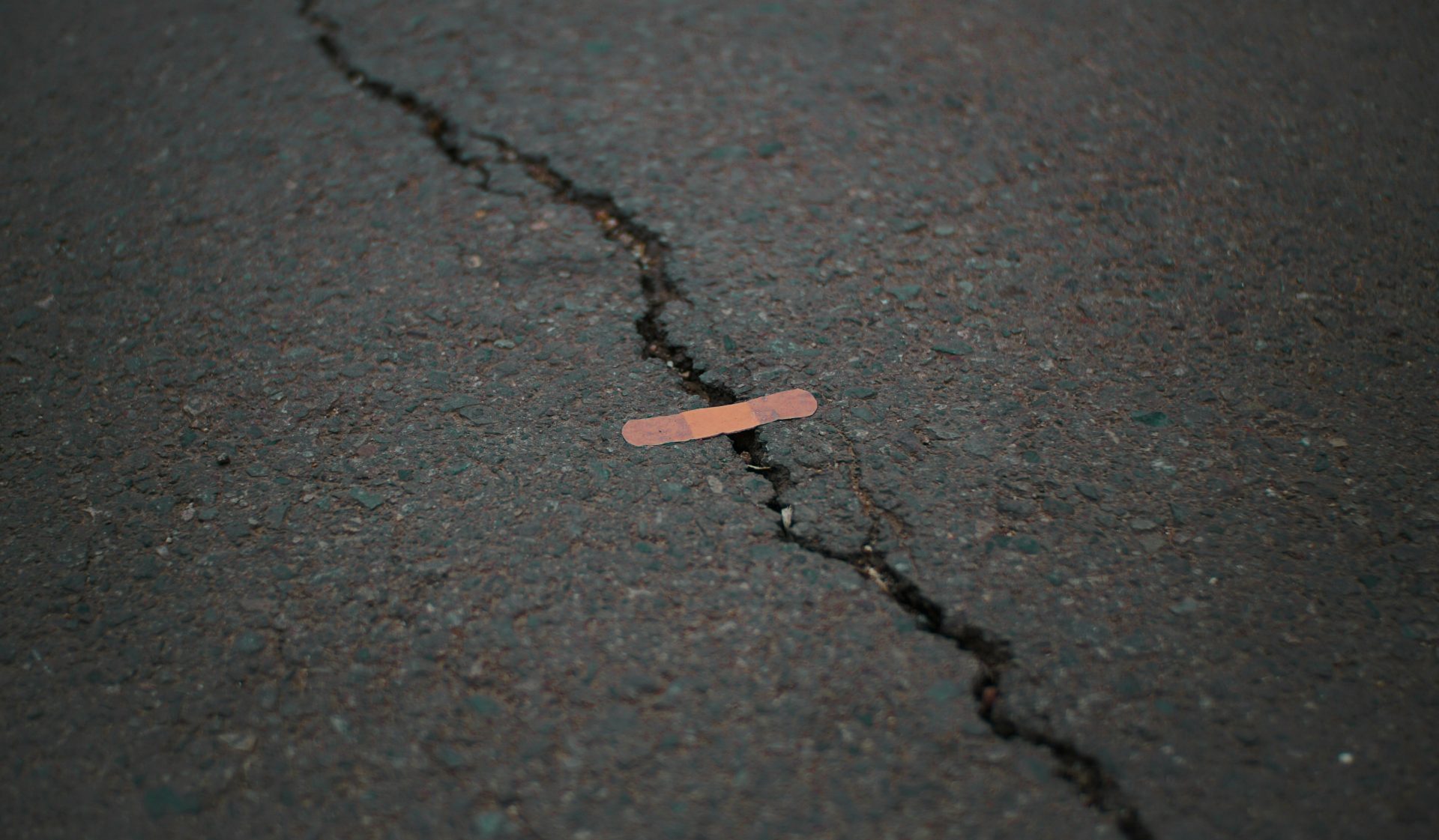 A big crack in an asphalt road with a tiny band-aid across a small part of the gap.