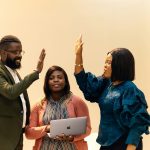 Two people high-fiving each other celebrating a success with a woman between them (all African American professionals )