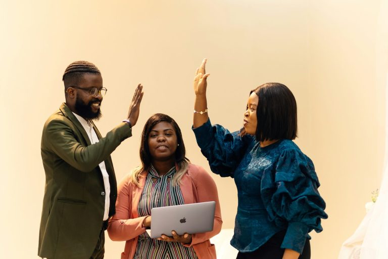 Two people high-fiving each other celebrating a success with a woman between them (all African American professionals )
