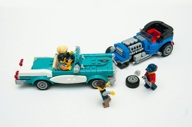 Two collided lego cars with the driver of one repairing a tire