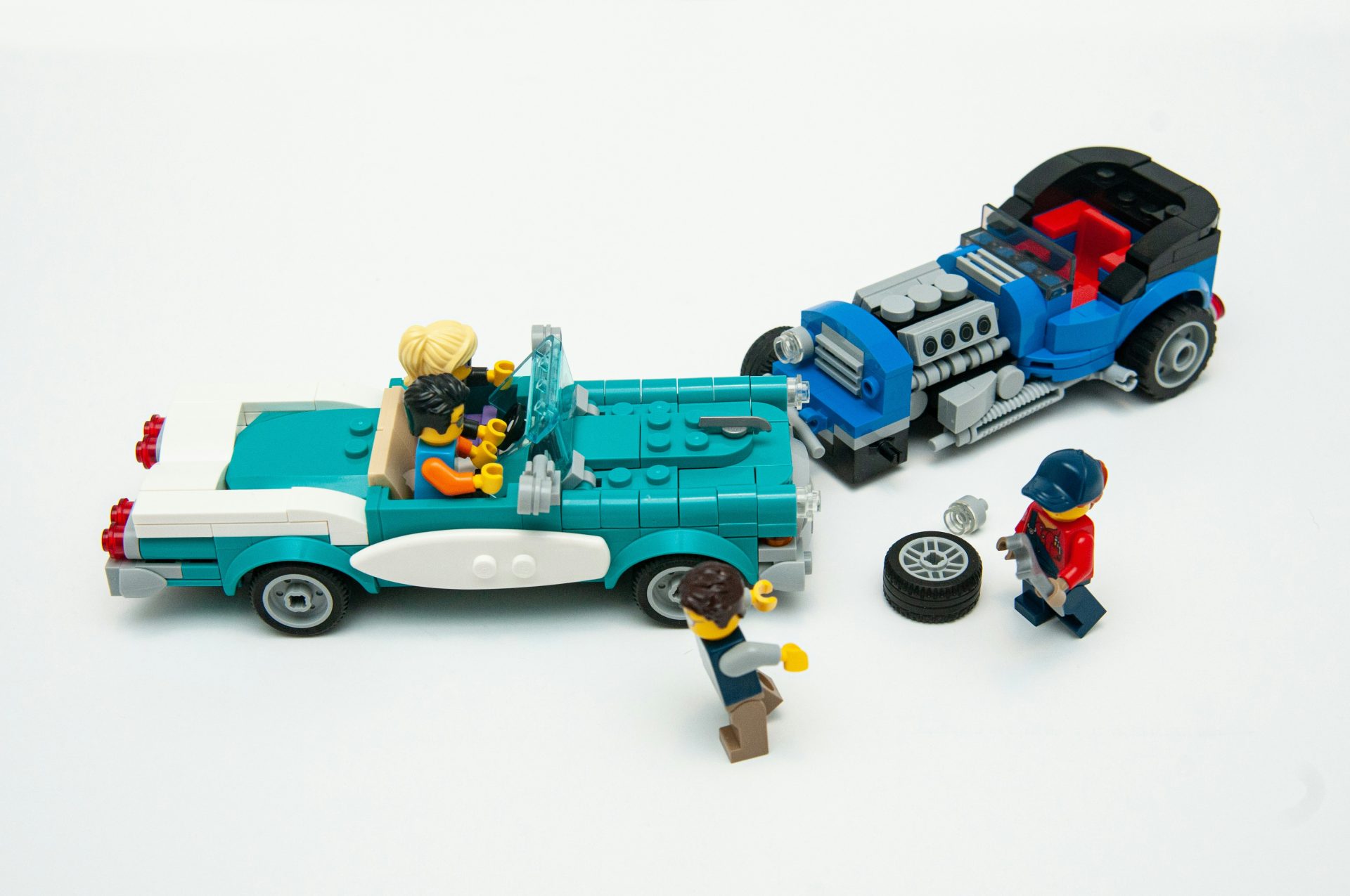 Two collided lego cars with the driver of one repairing a tire