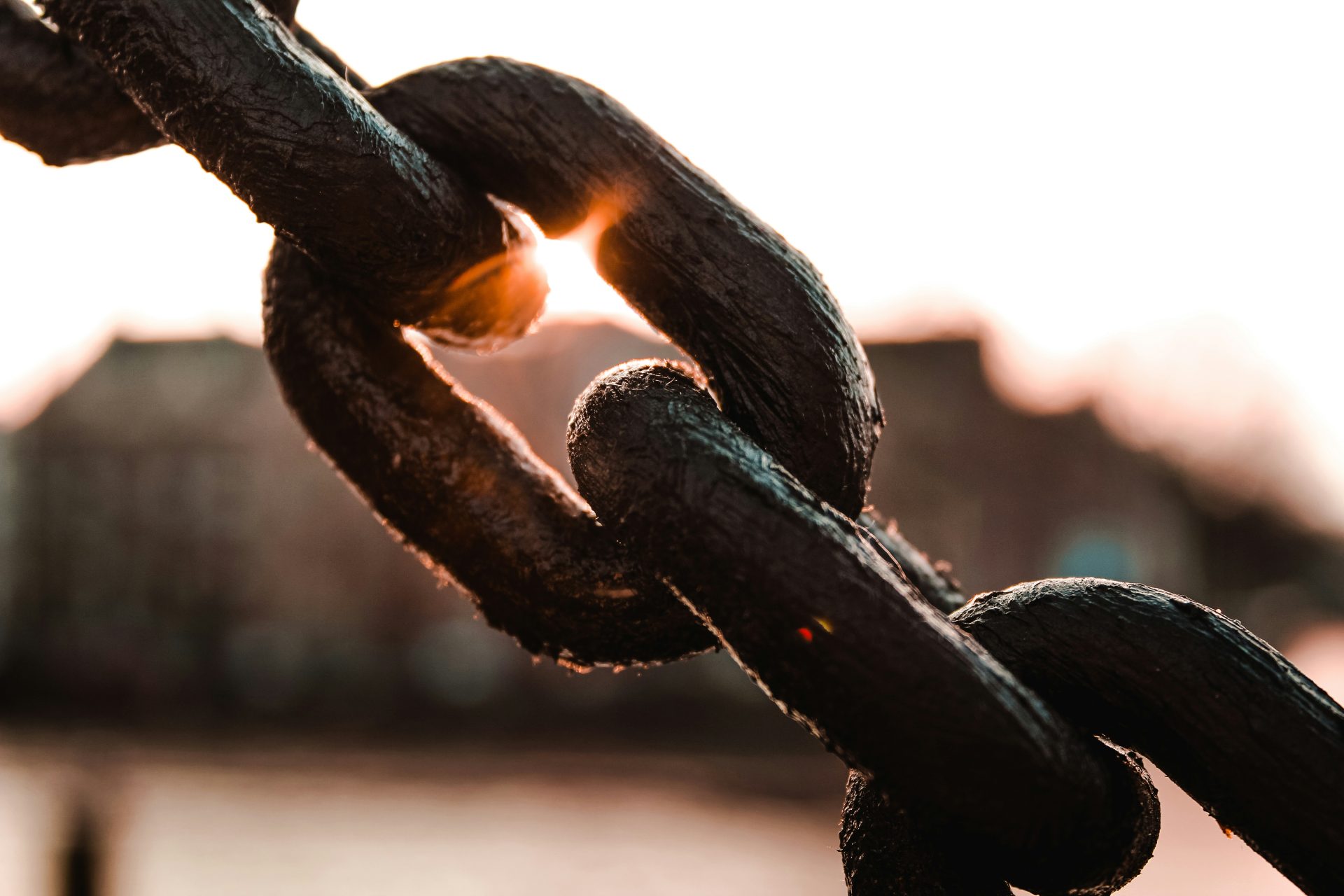 Close-up of 3 chain links in silhouette with sunlight shining from behind one of the links