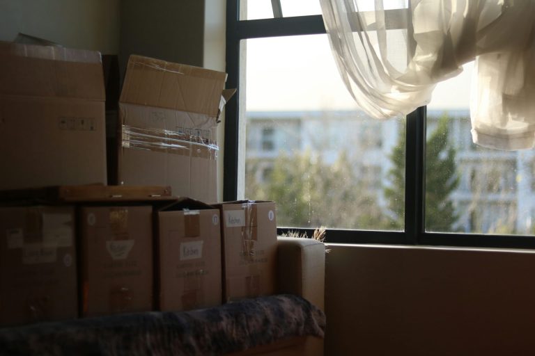 A stack of moving boxes tucked in a dark corner of room next to a window