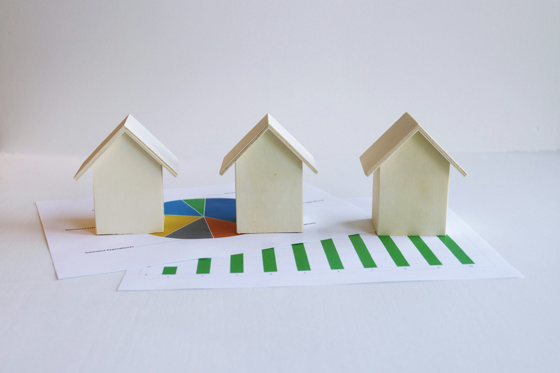 3 simple models of small wooden homes on top of a couple of spreadsheet charts - a pie chart and a bar chart