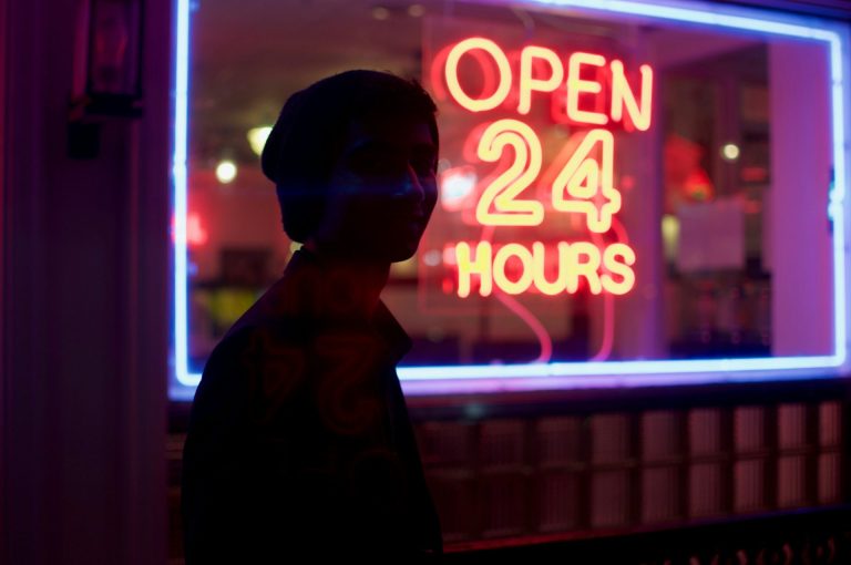 A neon frame sign at night "Open 24 Hours" with a silhouette of a person in front