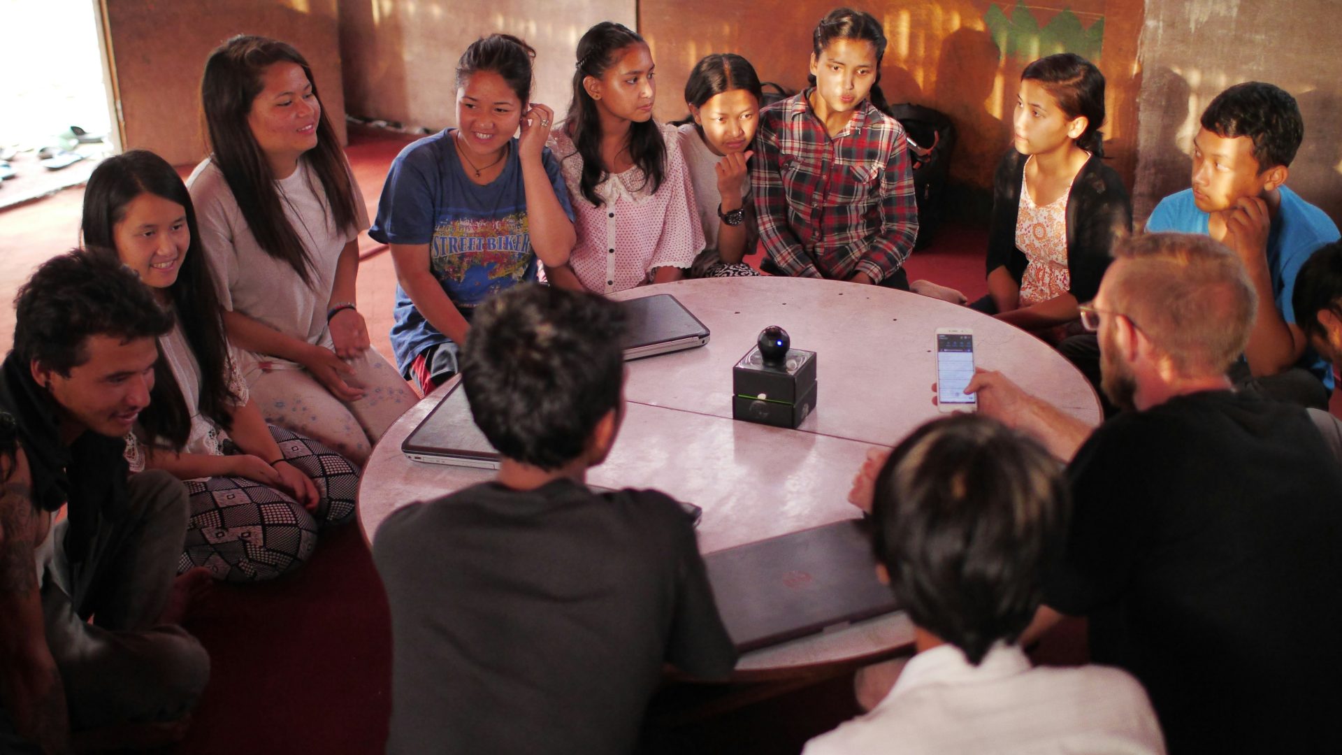 A large group of kids and a couple of teachers sitting around a table