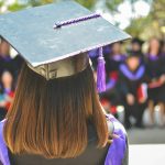Rear view of person with long hair at graduation ceremony with formal cap and gown.