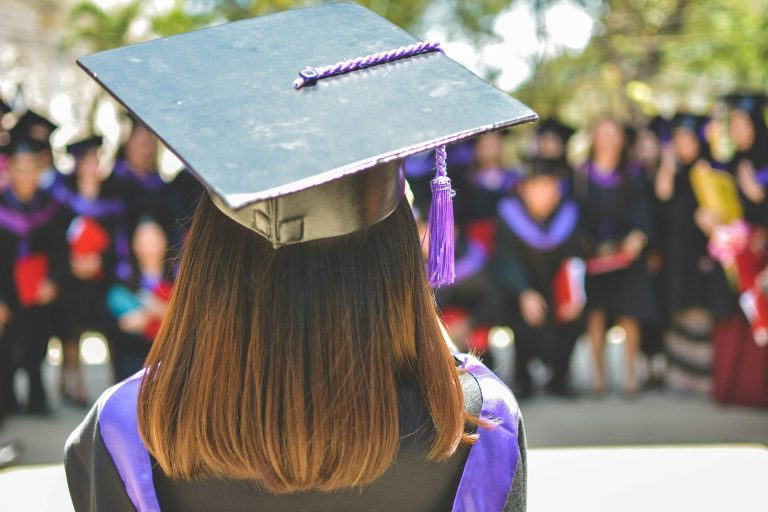 Rear view of person with long hair at graduation ceremony with formal cap and gown.