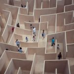Tiny people of all sorts (children, adults, families) wandering around in a massive maze