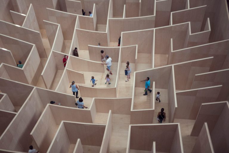 Tiny people of all sorts (children, adults, families) wandering around in a massive maze