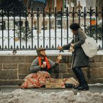 Woman giving a sandwich to a homeless man camped along the side of the street in the snow