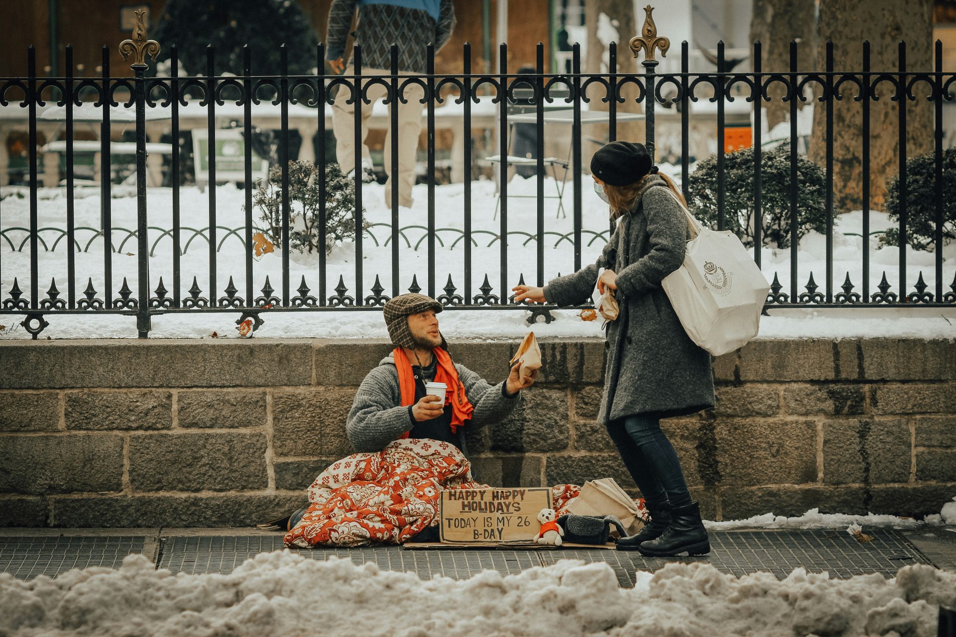 Woman giving a sandwich to a homeless man camped along the side of the street in the snow