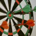 Dartboard with multiple green and red darts. One Green dart hits the bullseye.