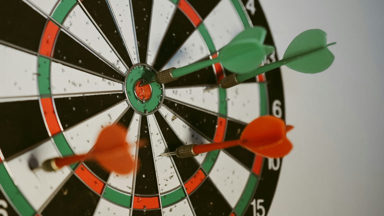 Dartboard with multiple green and red darts. One Green dart hits the bullseye.