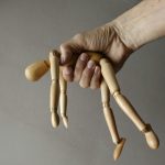 Close up of a hand holding a wooden mannequin